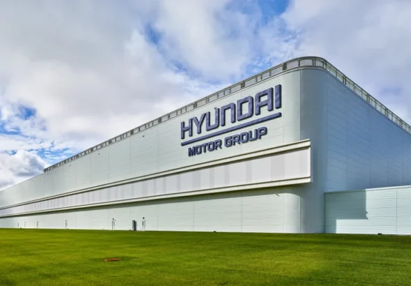 a-corner-of-an-enormous-low-white-building-is-visible-against-a-blue-sky-with-white-swirling-clouds-and-green-grass-in-the-fore