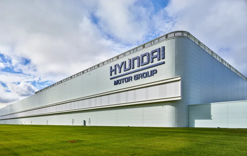 a corner of an enormous low white building is visible against a blue sky with white swirling clouds and green grass in the fore